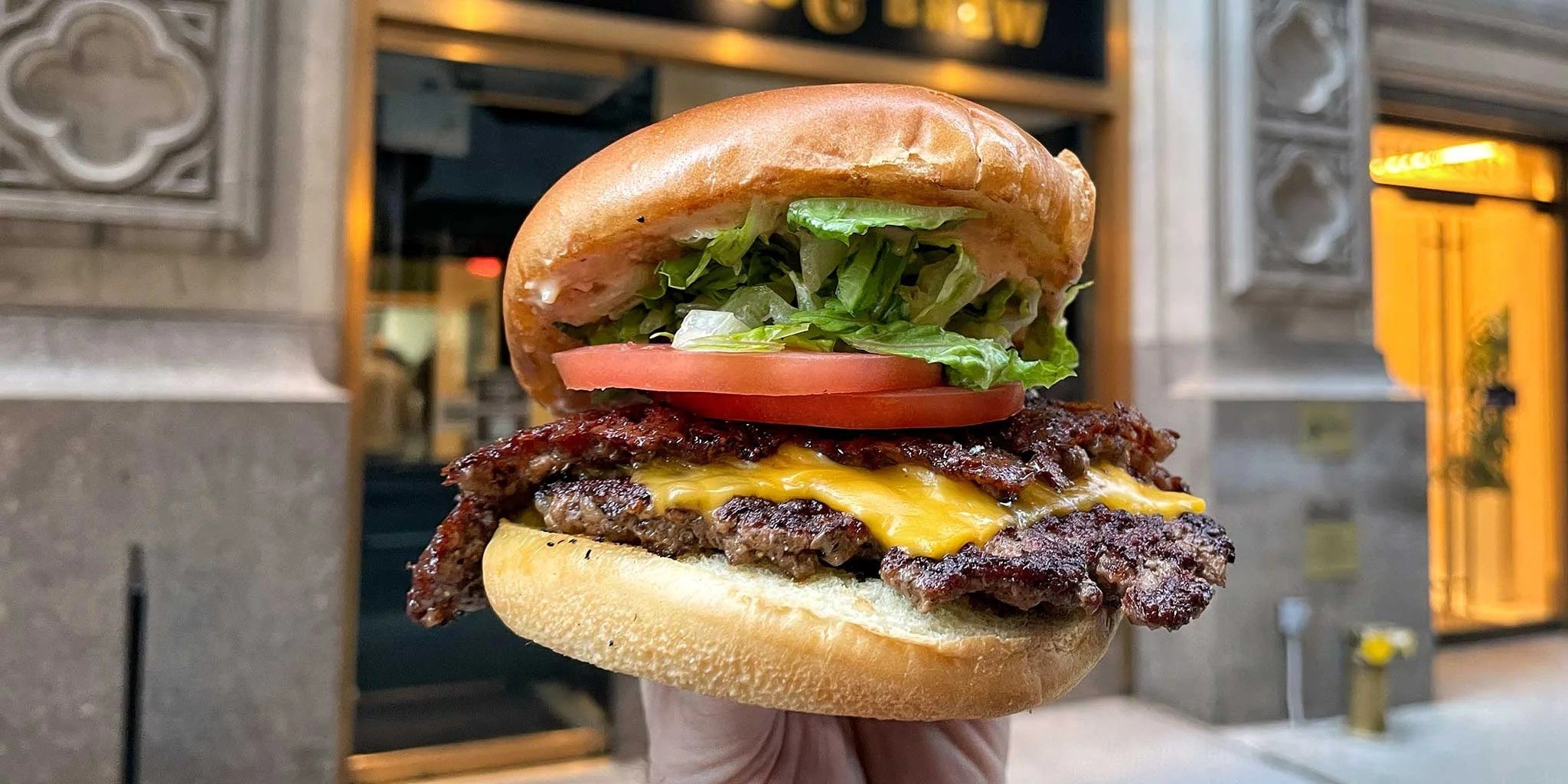 A double smash cheeseburger held up on the street outside Handcraft